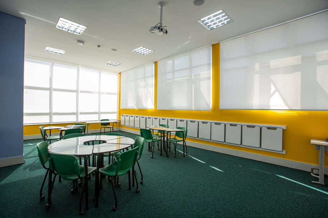 Sala de aula iluminada, com carteiras organizadas e quadro ao fundo