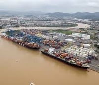 Complexo portuário com navios e guindastes em operação ao pôr do sol.