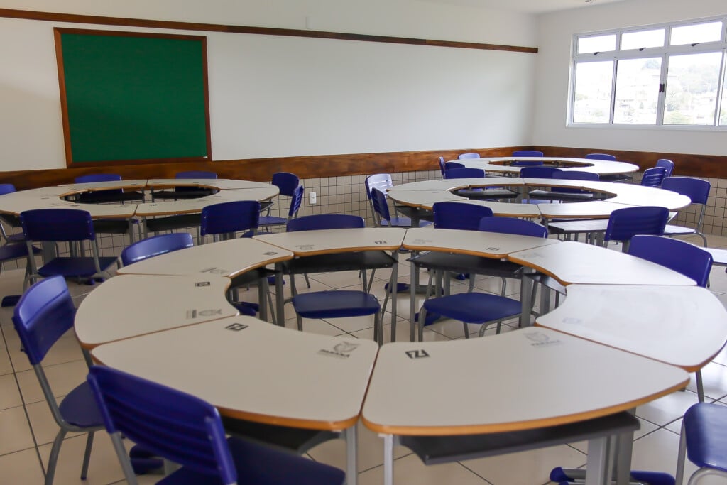 Sala de aula moderna com mesas e cadeiras azuis, bem iluminada, com quadro na parede