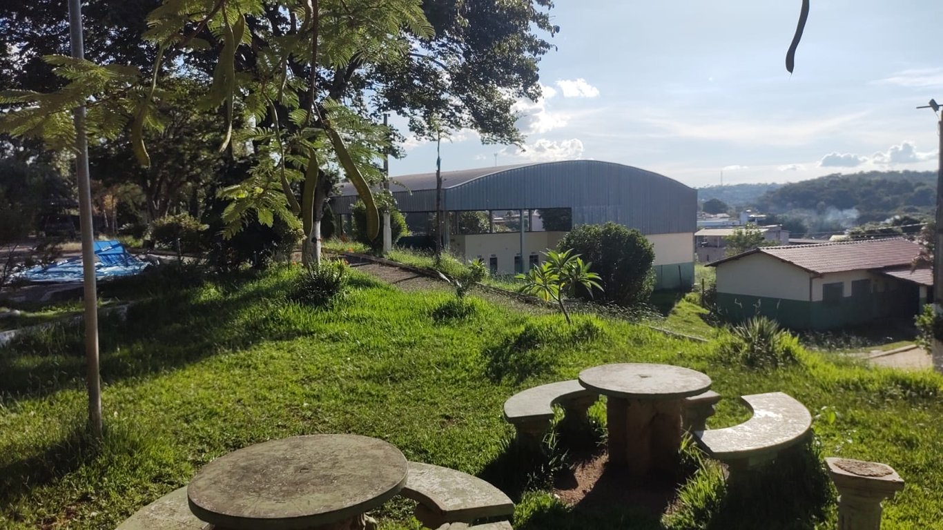 Ambiente escolar ao ar livre, com mesas de pedra e vegetação, em perspectiva horizontal