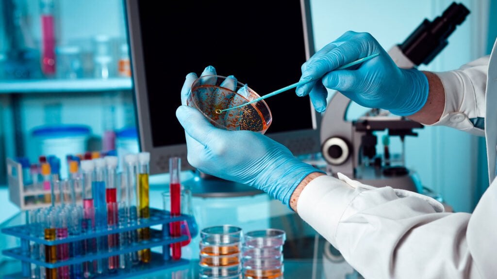 Ambiente acadêmico de laboratório de microbiologia, com bancada, microscópios e placas de Petri