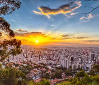 Belo Horizonte MG ao pôr do sol, com prédios e a Serra do Curral ao fundo.