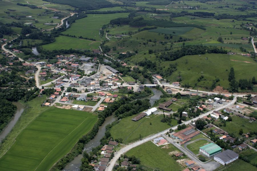 Vista aérea de Mirim Doce SC, com casas e colinas verdes ao redor, céu limpo