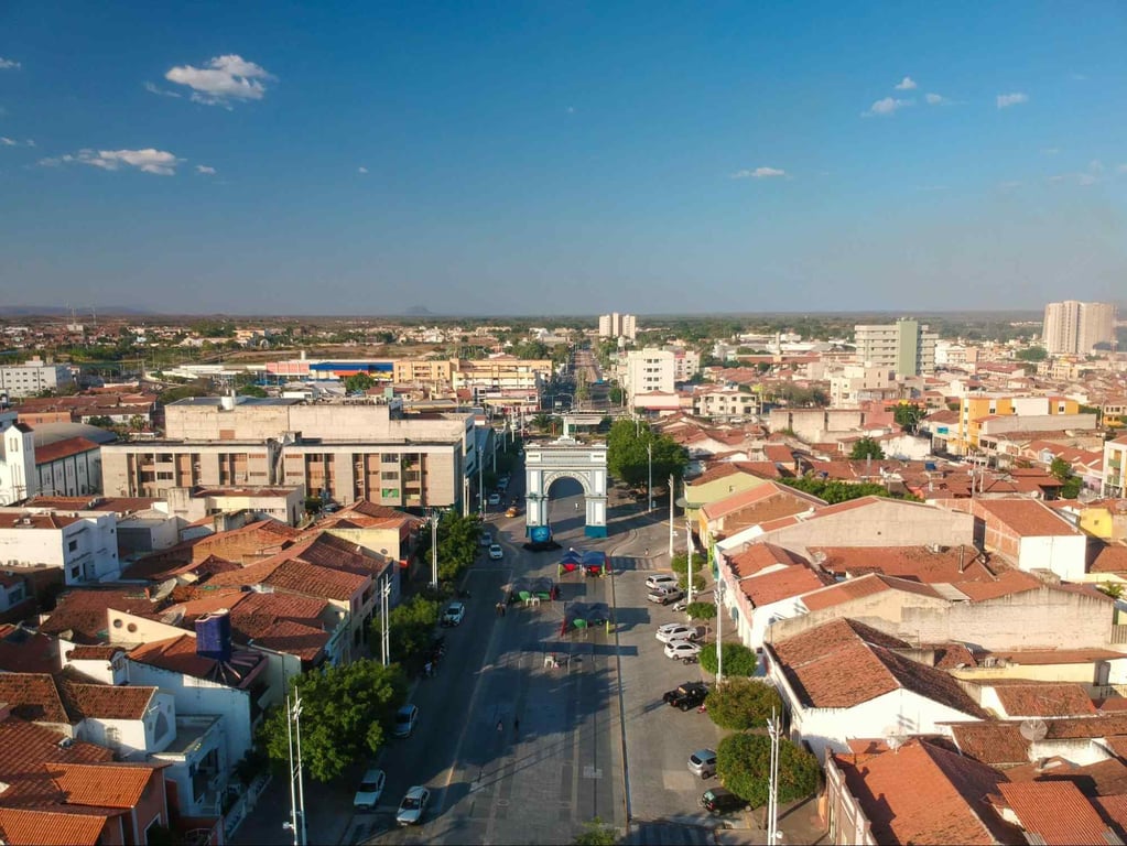 Paisagem urbana no interior do Nordeste, em composição horizontal, com casario e área verde ao fundo
