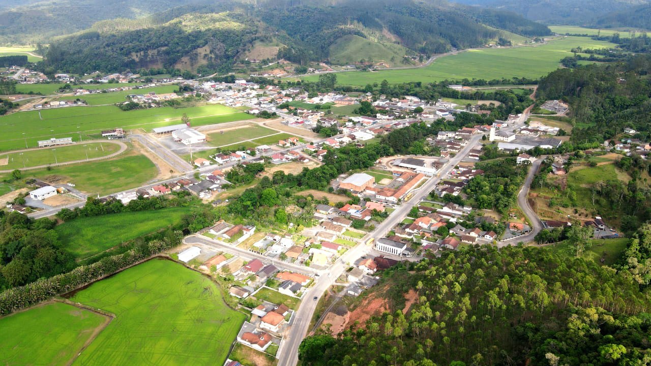 Vista aérea do interior de Santa Catarina, com cidade cercada por morros e áreas verdes