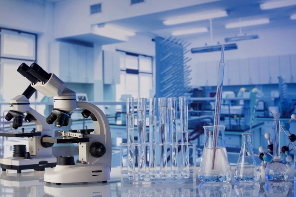Laboratório de química com microscópios e vidrarias em bancadas, iluminação natural e ambiente organizado