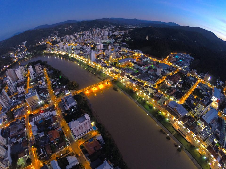 Vista aérea de Sombrio SC ao entardecer, com área urbana, rio e montanhas ao fundo