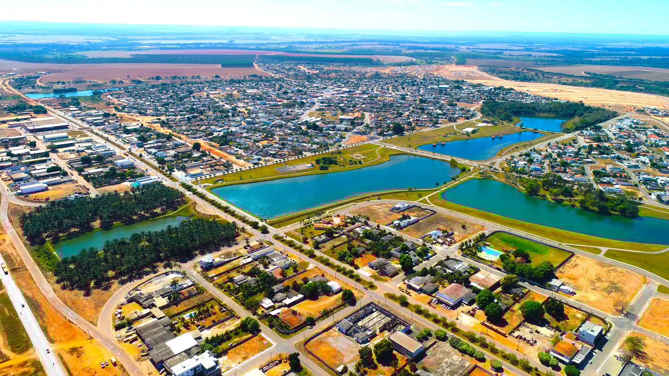 Região norte de Mato Grosso; paisagem urbana com lago e vegetação, representando cidades do eixo da BR-163.