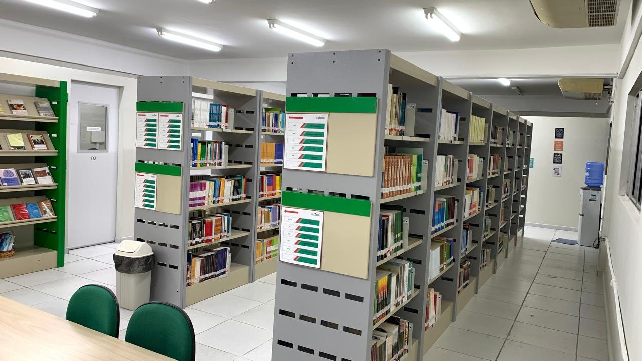 Interior de biblioteca universitária com estantes de livros e mesas de estudo