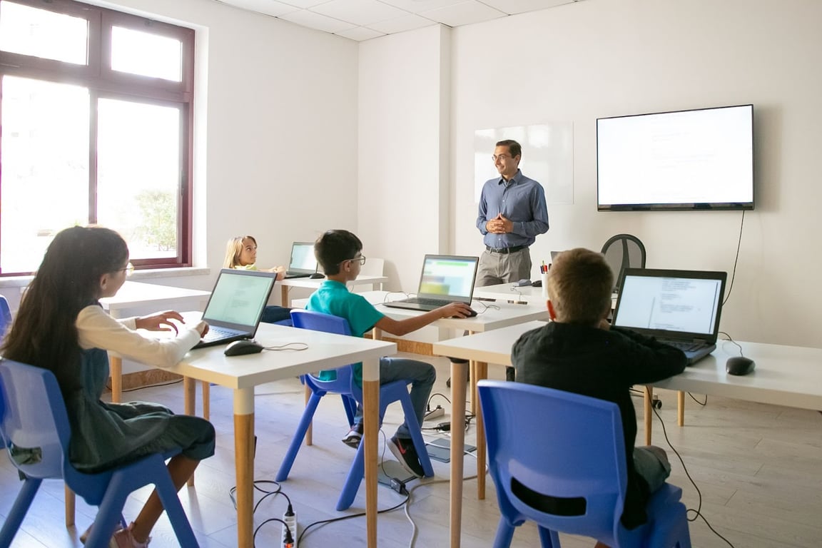 Sala de aula em curso superior, com professor e alunos usando laptops