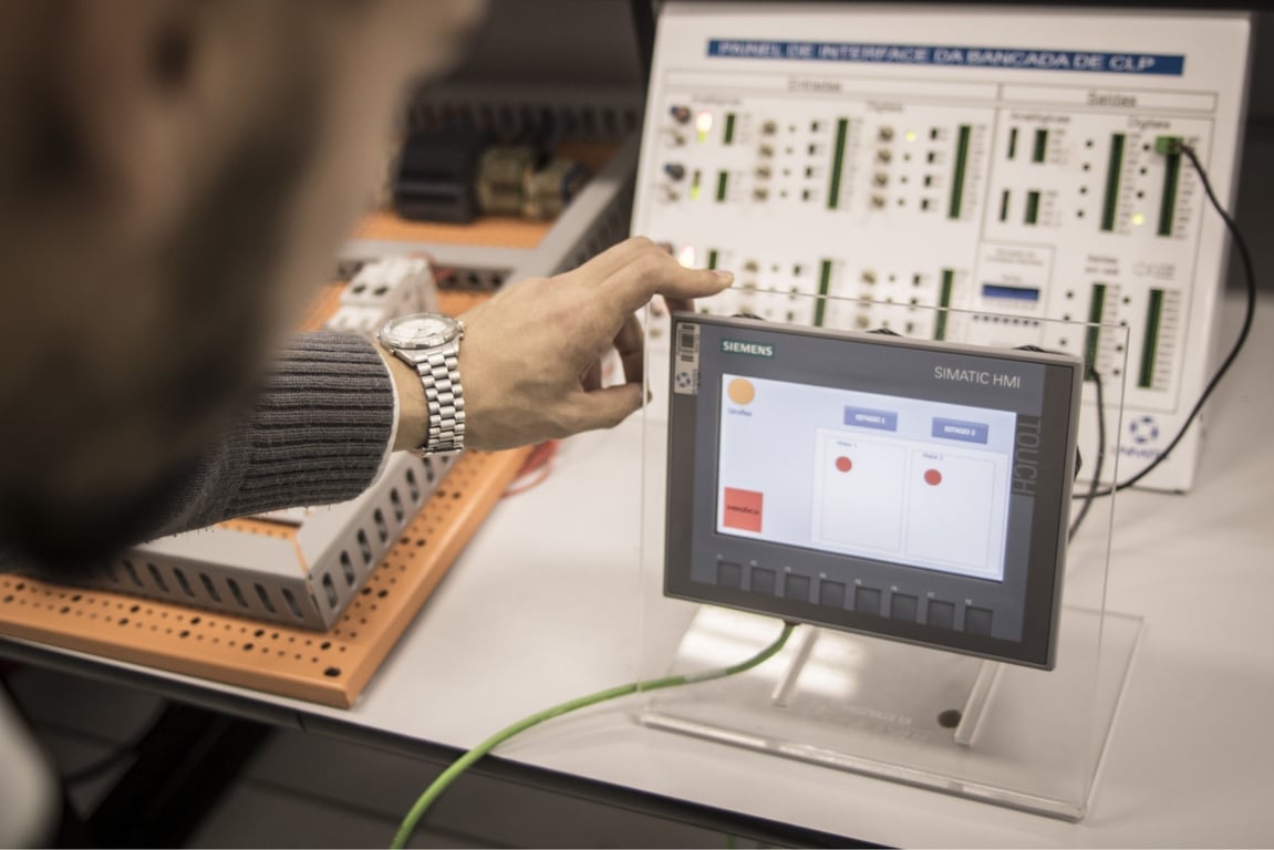 Ambiente acadêmico de automação industrial, com painéis, CLPs e operação em bancada