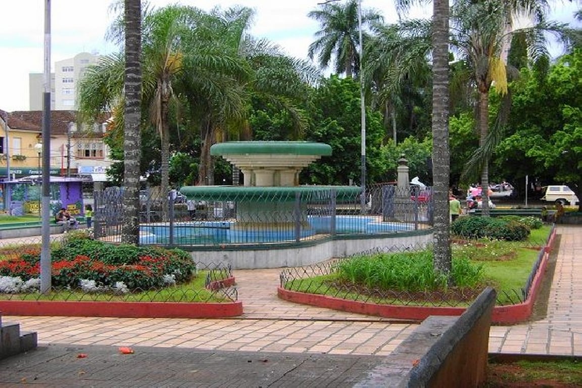 Praça central arborizada com fonte e prédios ao fundo em Alfenas MG