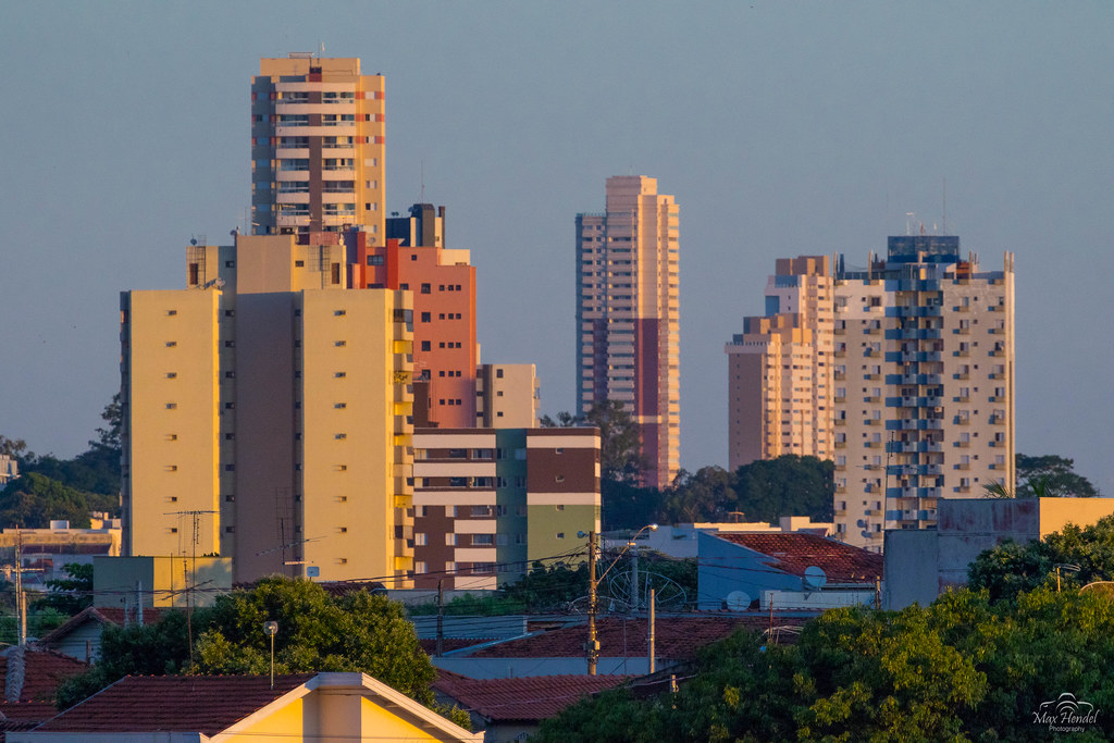 Skyline central de Bauru SP ao entardecer, com prédios e vegetação, em composição horizontal