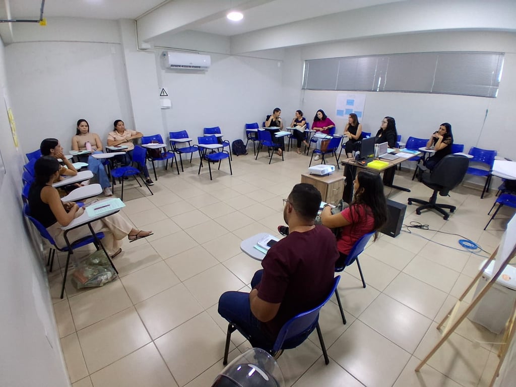 Sala de aula em instituição pública, com estudantes e professor ao fundo, representando a rotina docente