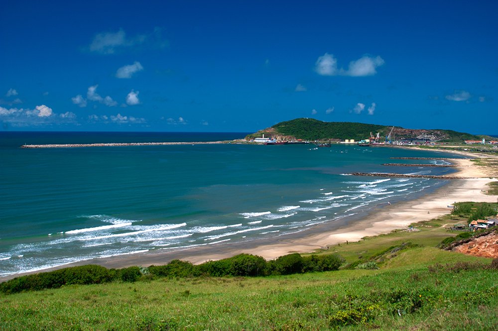 Vista panorâmica do litoral sul catarinense, com vegetação costeira e lagoa ao fundo, sob céu limpo
