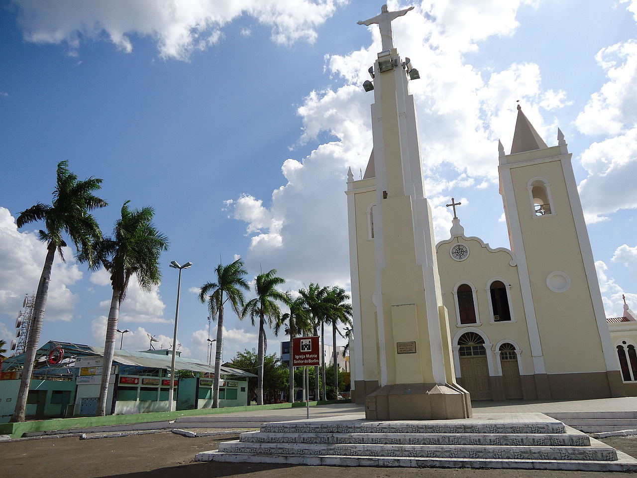 Praça central de Monsenhor Tabosa CE com igreja ao fundo, céu azul e vegetação de praça
