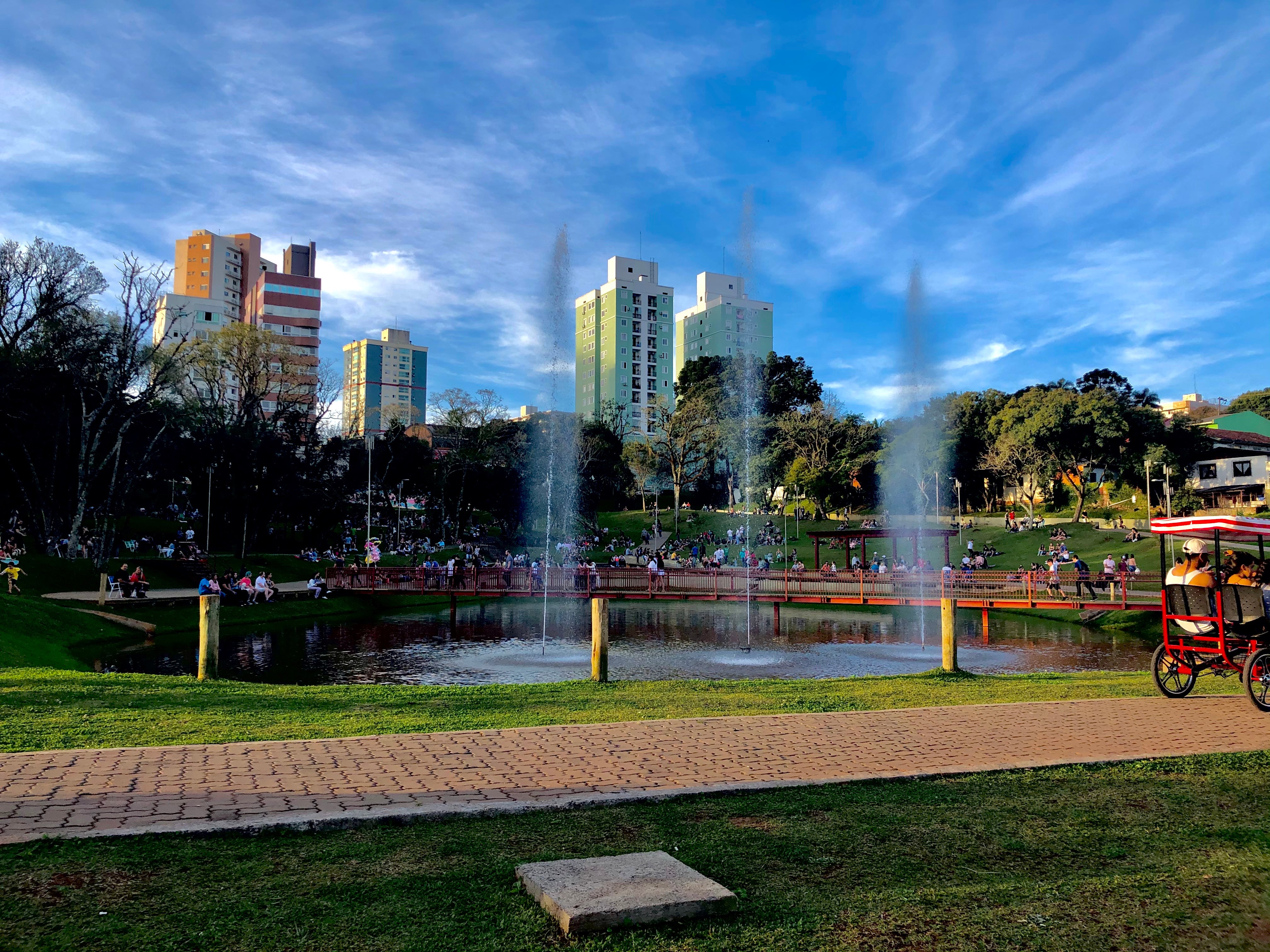 Centro urbano de cidade do interior, com parque e prédios ao fundo, em dia ensolarado