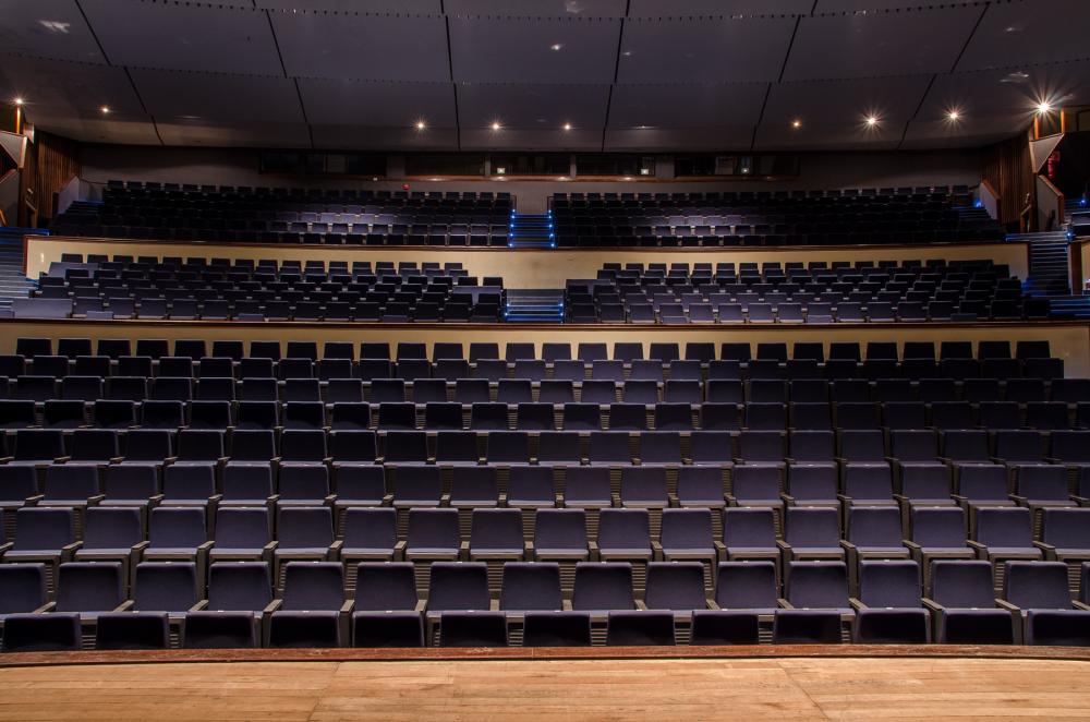 Auditório universitário, cadeiras alinhadas e palco ao fundo, em perspectiva horizontal