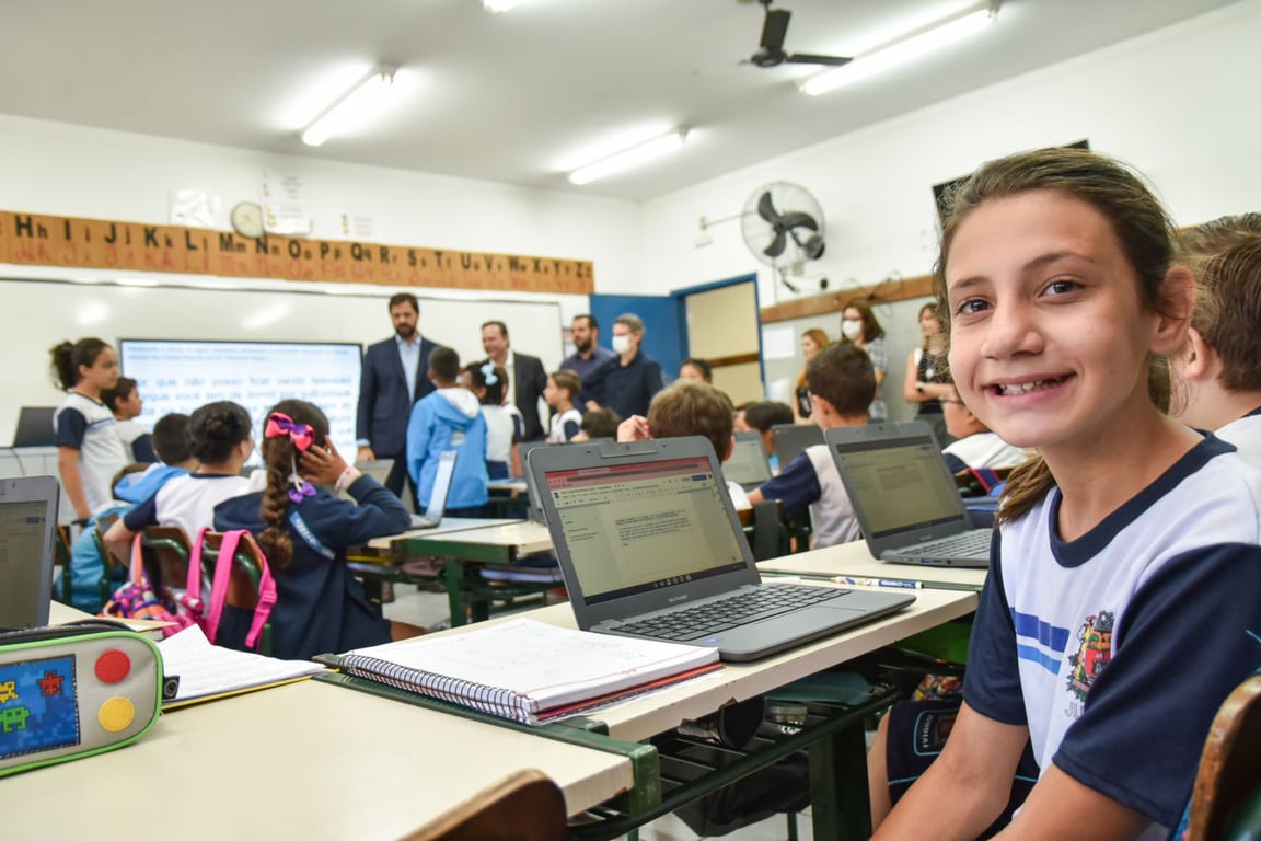 Sala de aula de escola pública com professor e alunos, ambiente iluminado e organização que remete à educação básica