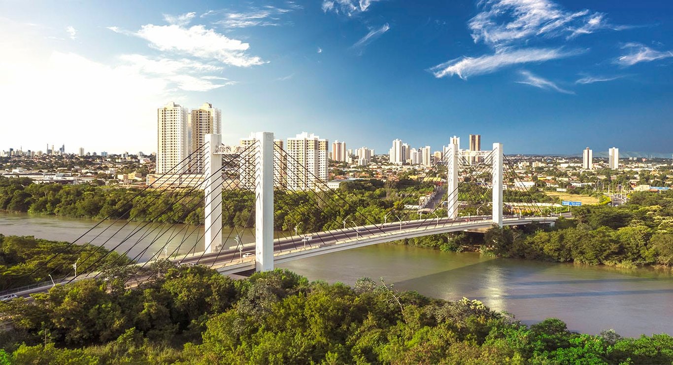 Horizonte de Cuiabá ao entardecer, com ponte sobre o rio e prédios ao fundo
