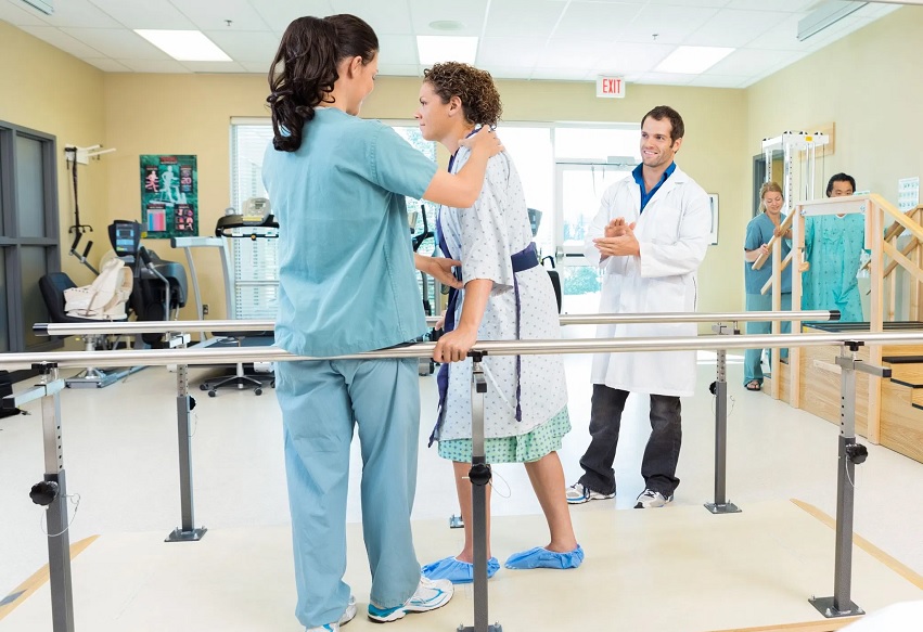 Equipe multiprofissional em sessão de reabilitação hospitalar, auxiliando paciente
