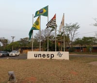 Entrada do campus da UNESP em Bauru SP com bandeiras e nome da instituição.