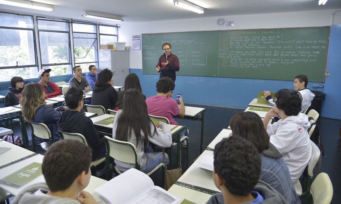 Sala de aula pública com professor e estudantes, em composição horizontal