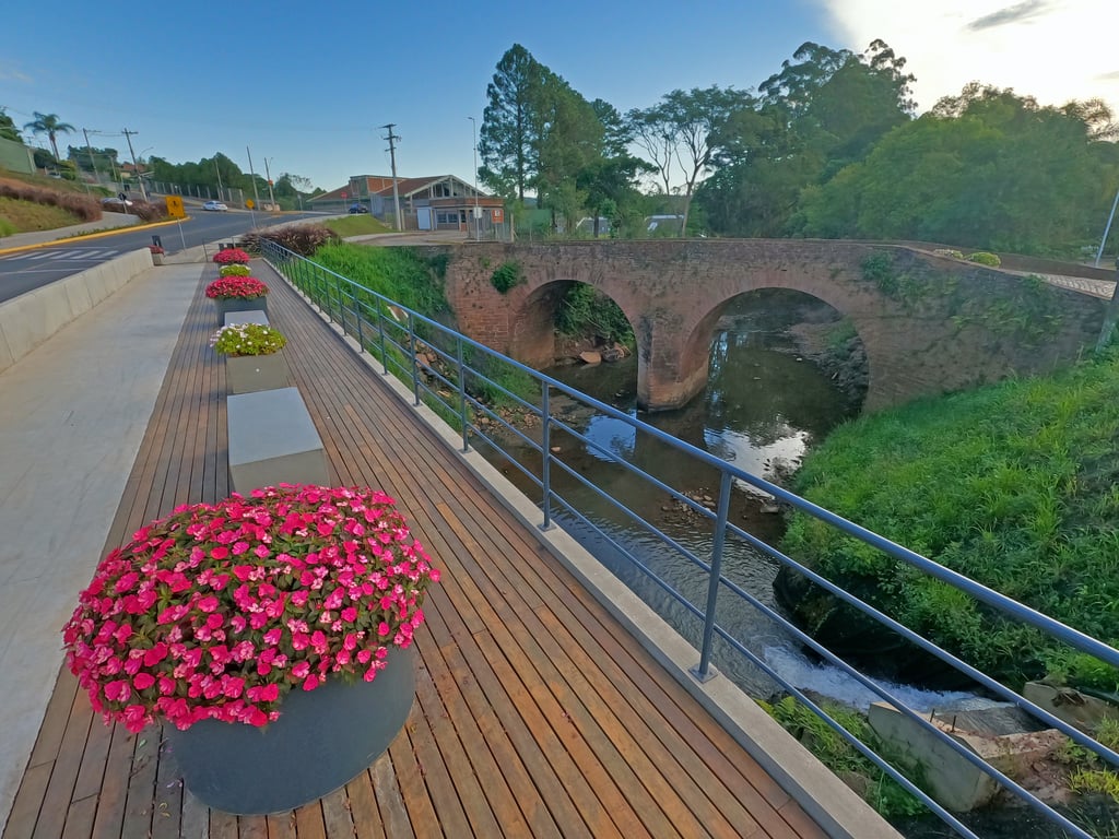 Vista urbana de Presidente Lucena RS, com ponte de pedra sobre o rio e vegetação ao redor