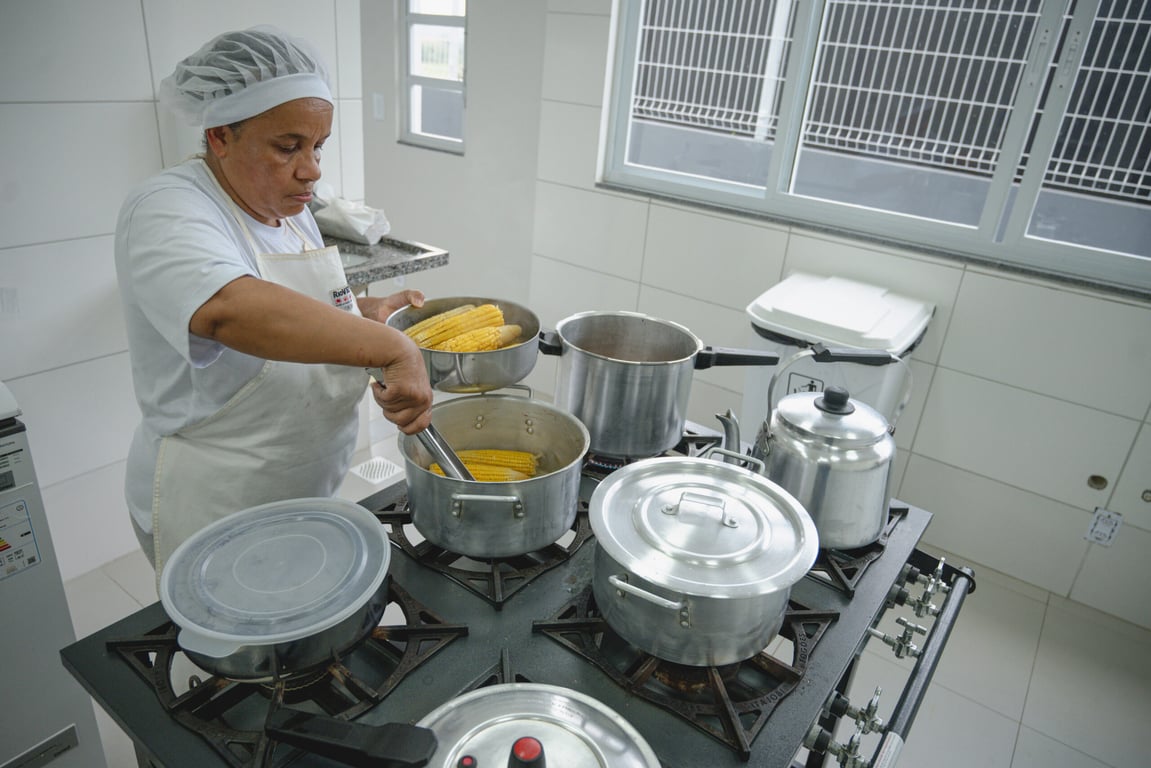 Rotina em cozinha escolar, com merendeira preparando alimentos