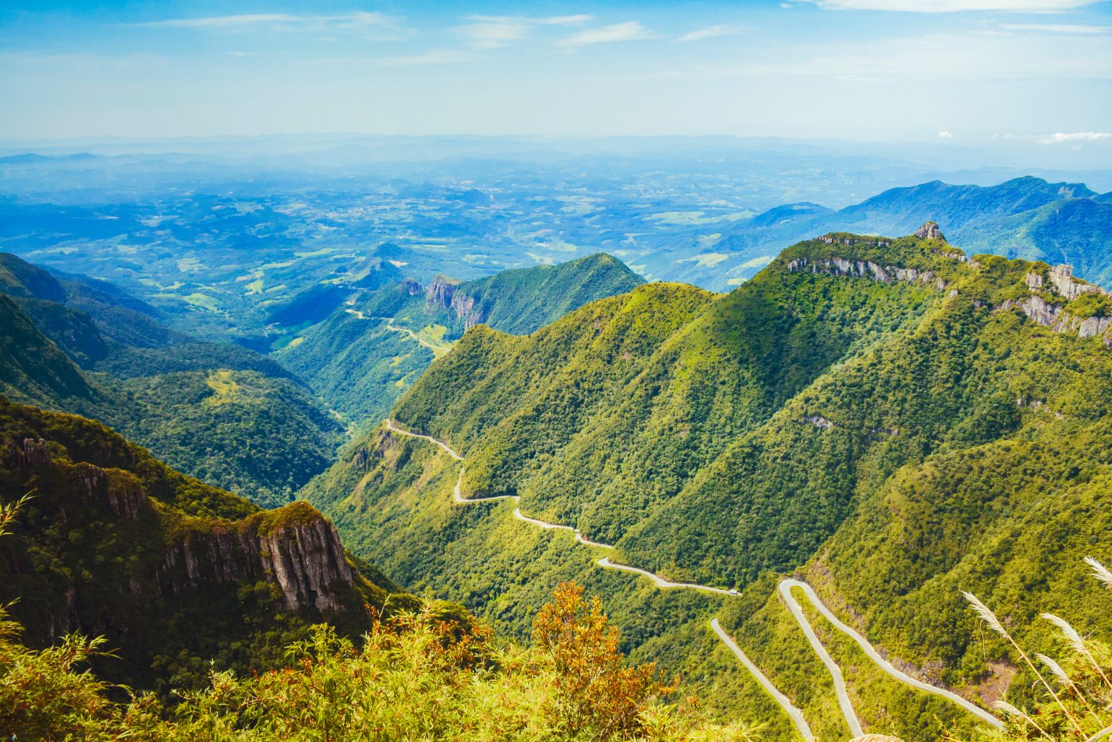 Estrada sinuosa entre campos e morros no interior do RS, vista aérea em dia ensolarado