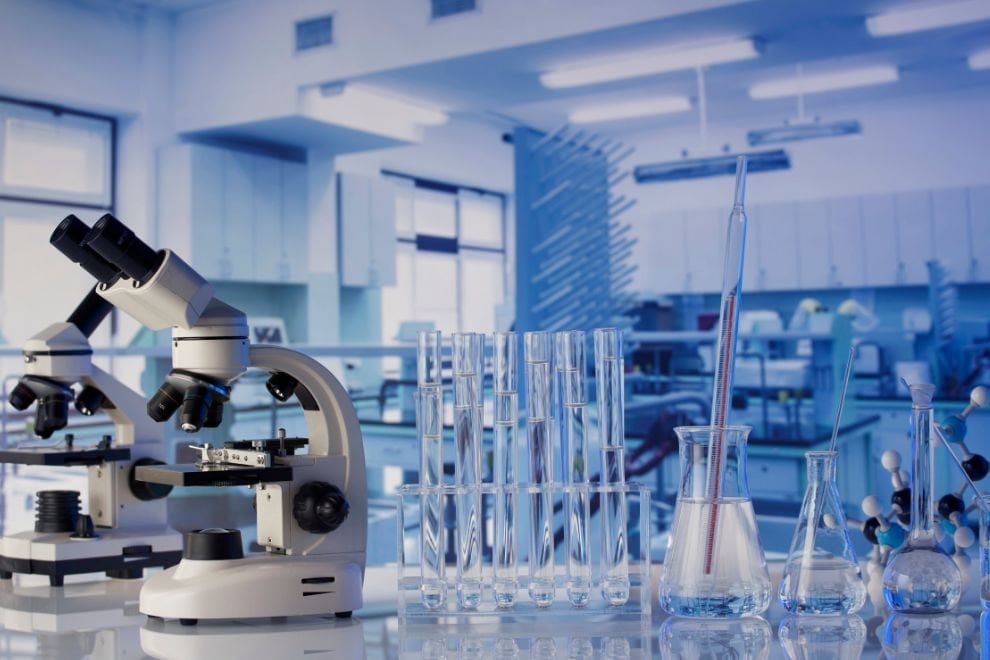 Laboratório científico com microscópios e vidrarias sobre bancada, ambiente educacional moderno