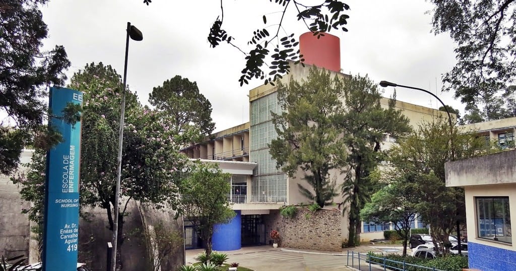 Fachada da Escola de Enfermagem da USP cercada por árvores, com céu nublado.