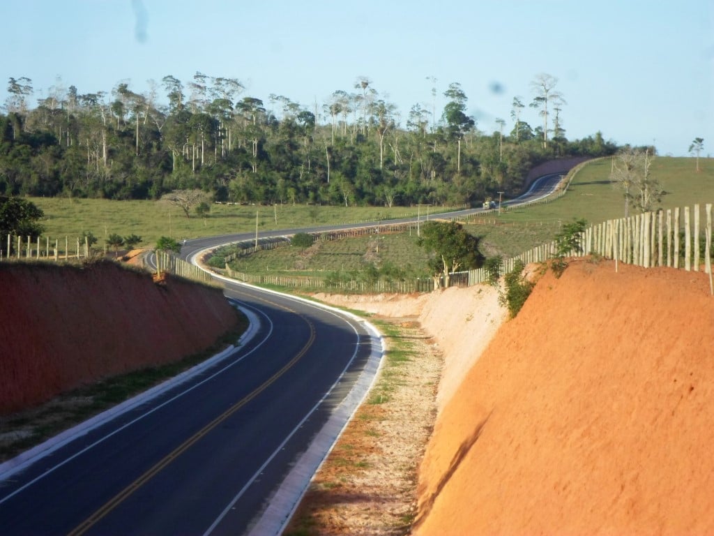 Equipe operando máquina de pavimentação em rodovia, com relevo montanhoso ao fundo.