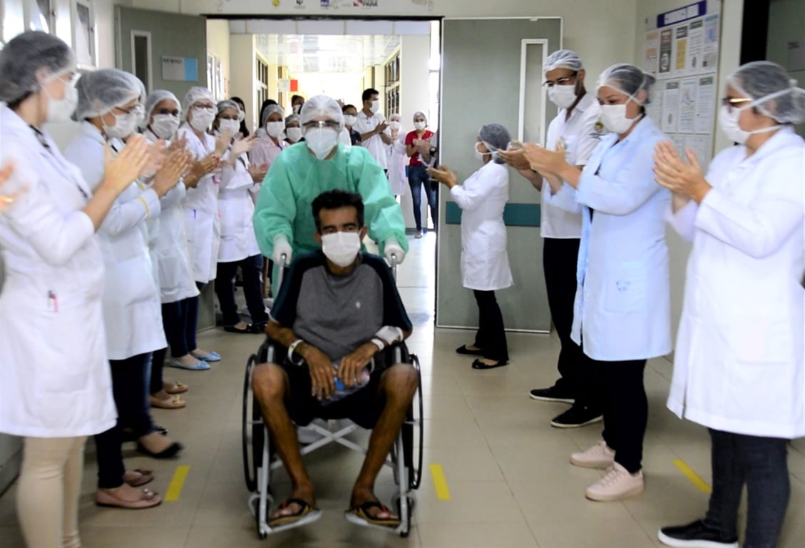 Profissionais de saúde em corredor de hospital público, aplaudindo paciente