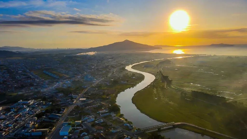 Vista aérea de uma cidade costeira com rio e morros verdes ao fundo