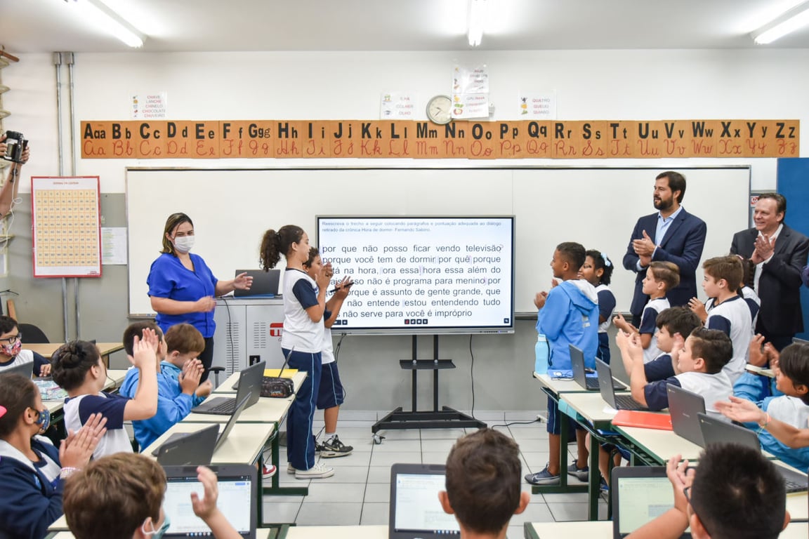 Sala de aula com estudantes utilizando laptops e quadro interativo