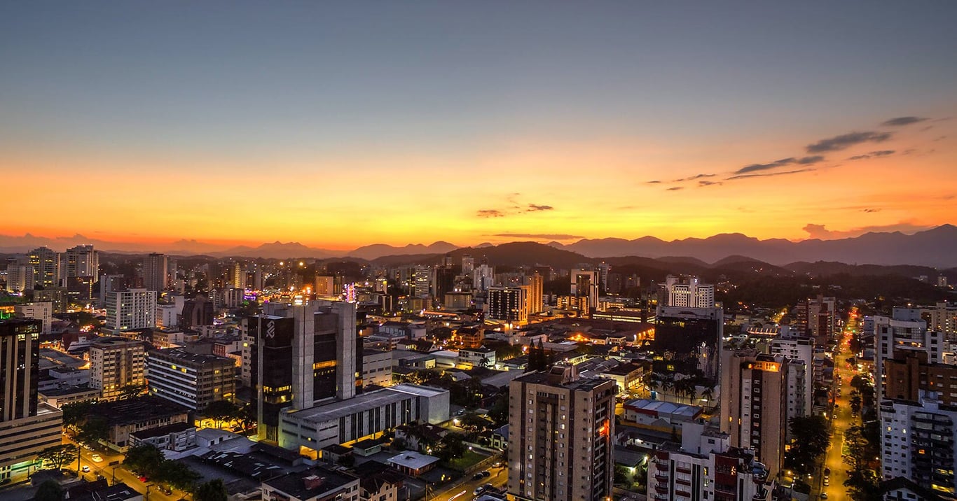 Panorama urbano de Joinville ao pôr do sol, com montanhas ao fundo