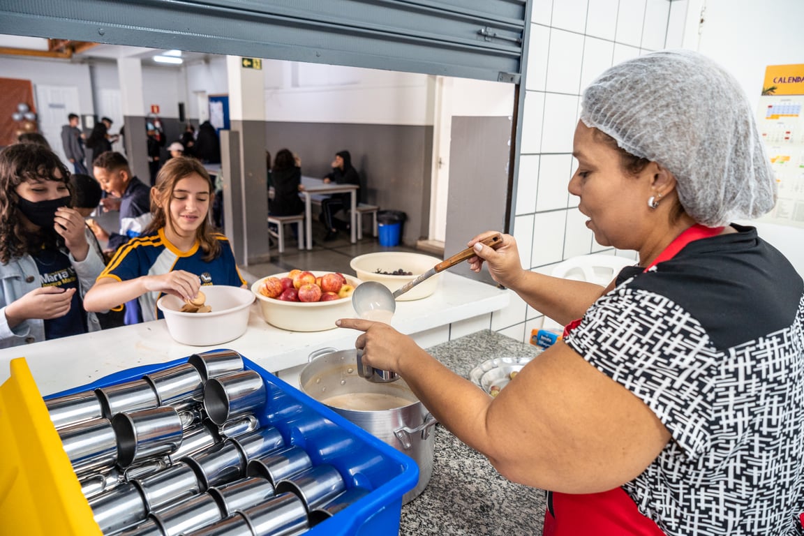 Refeitório escolar com servidora distribuindo a merenda