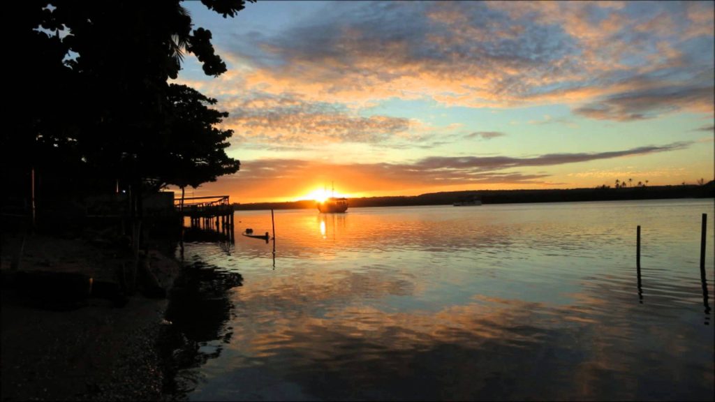 Lagoa Mundaú ao pôr do sol, com embarcações e margem urbana ao fundo