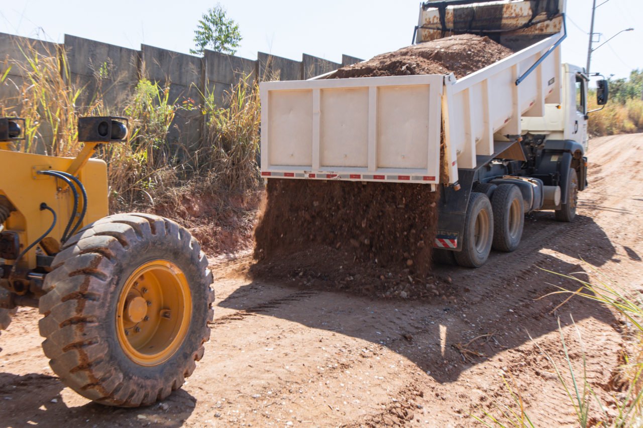 Caminhão basculante e motoniveladora em obra viária