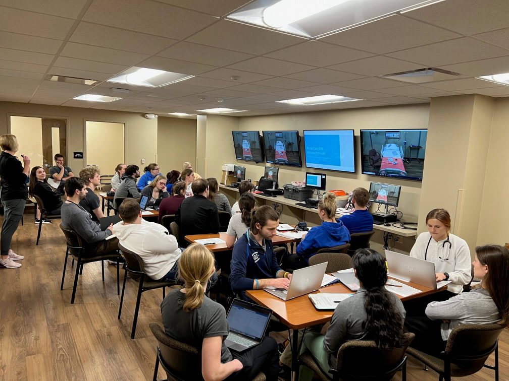 Ambiente de simulação/laboratório com profissionais e estudantes de enfermagem em atividade de aprendizagem