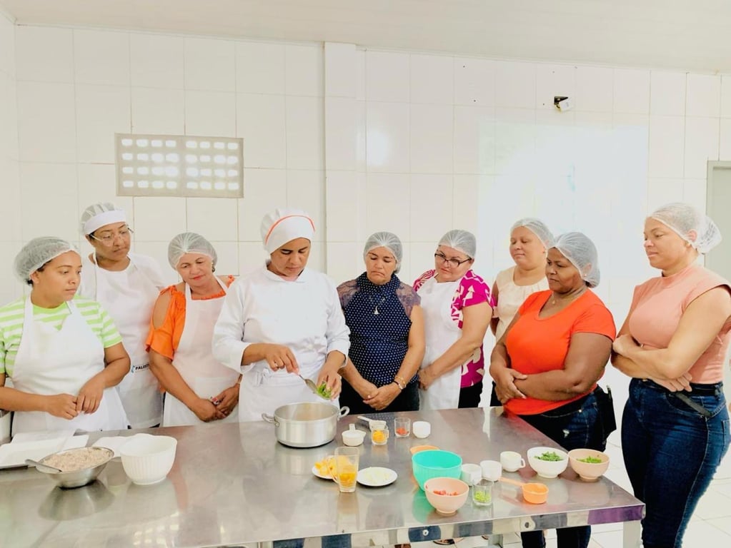 Merendeiras em cozinha escolar preparando refeições, foco nas mãos e no preparo