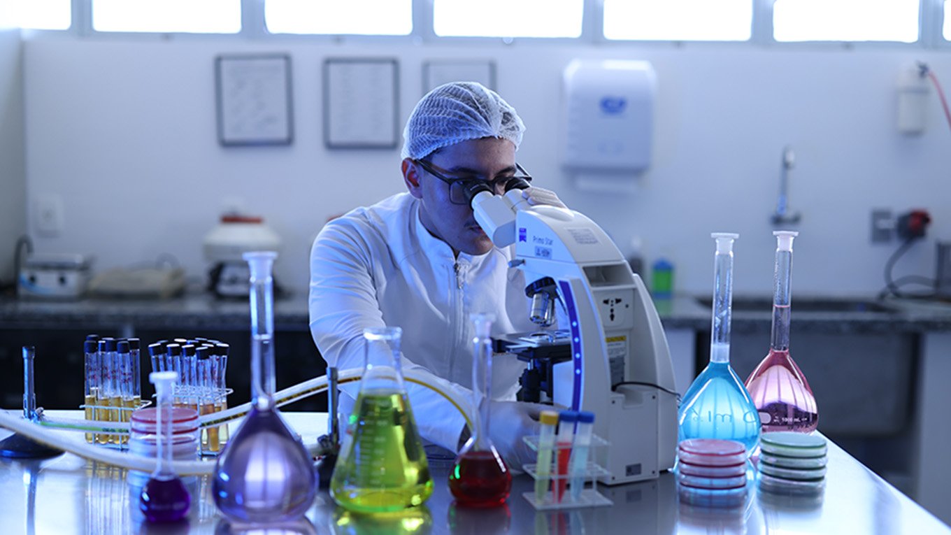 Pesquisador em laboratório biomédico, com microscópio e bancadas ao fundo