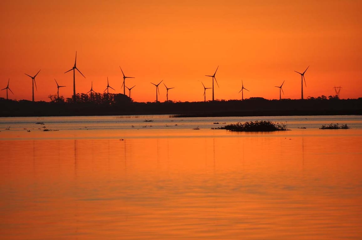 Parque eólico ao pôr do sol, com várias turbinas.