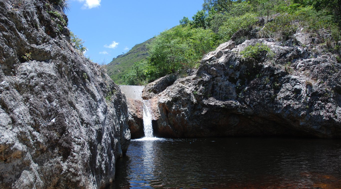 Cenário natural com pequeno curso d’água entre rochas e vegetação (imagem ilustrativa)