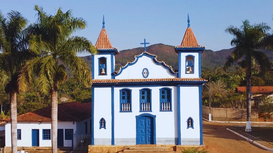 Centro de Leopoldina MG em dia ensolarado, com igreja e palmeiras ao fundo