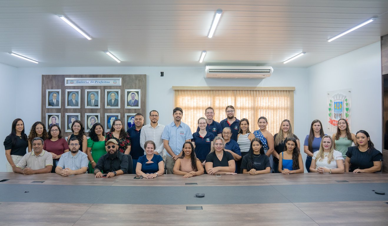 Servidores públicos municipais em ambiente institucional, em uma prefeitura, com retratos oficiais ao fundo