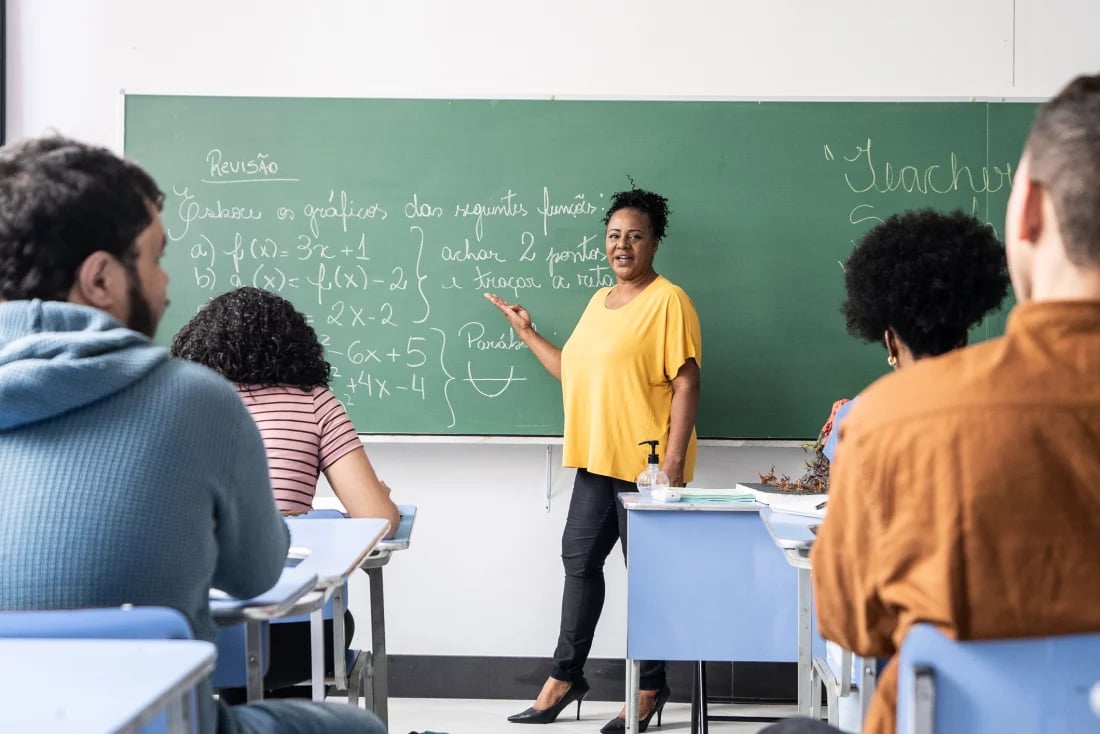 Sala de aula do ensino fundamental com professora no quadro e alunos atentos
