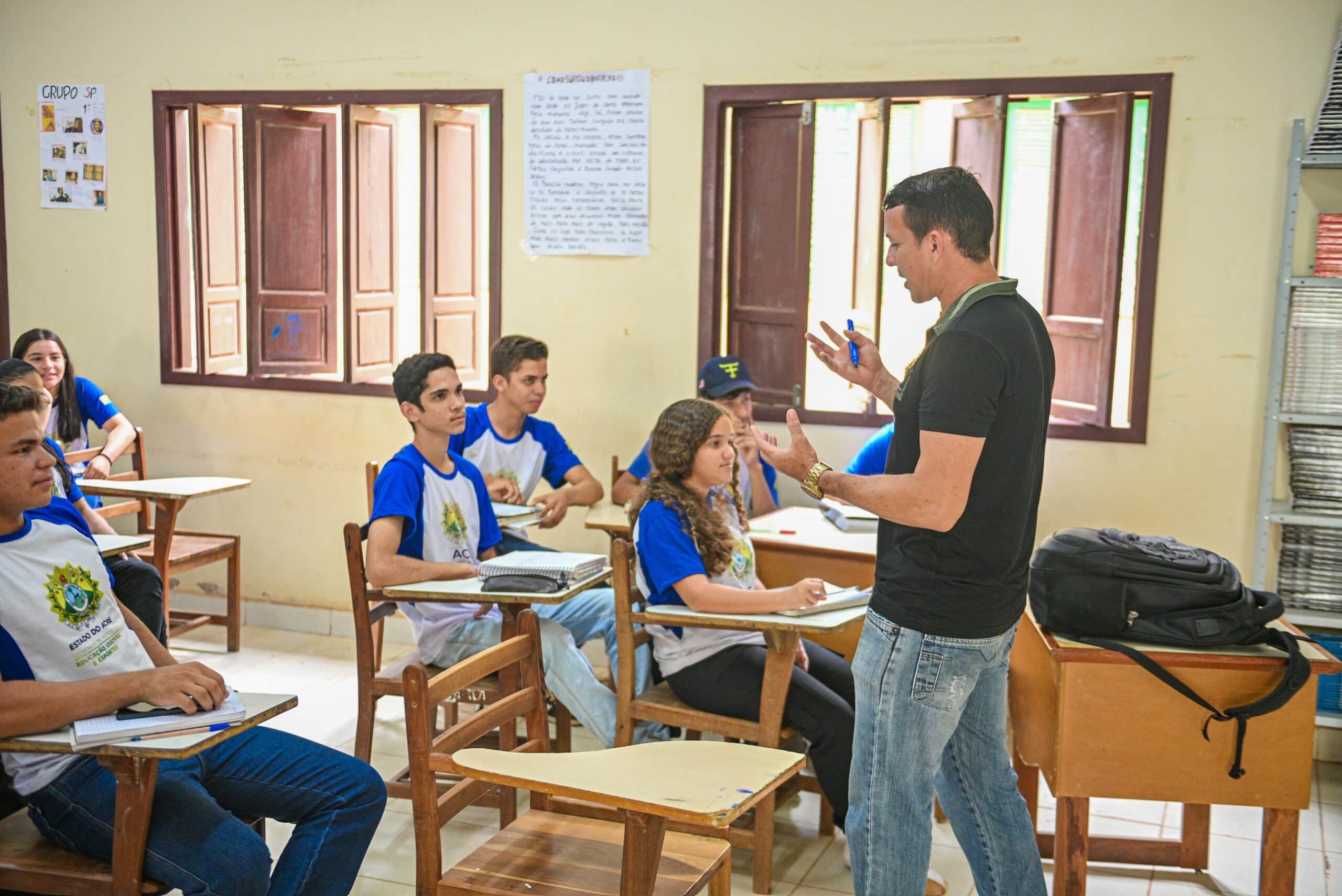 Professor em sala de aula com estudantes do ensino fundamental, quadro branco ao fundo