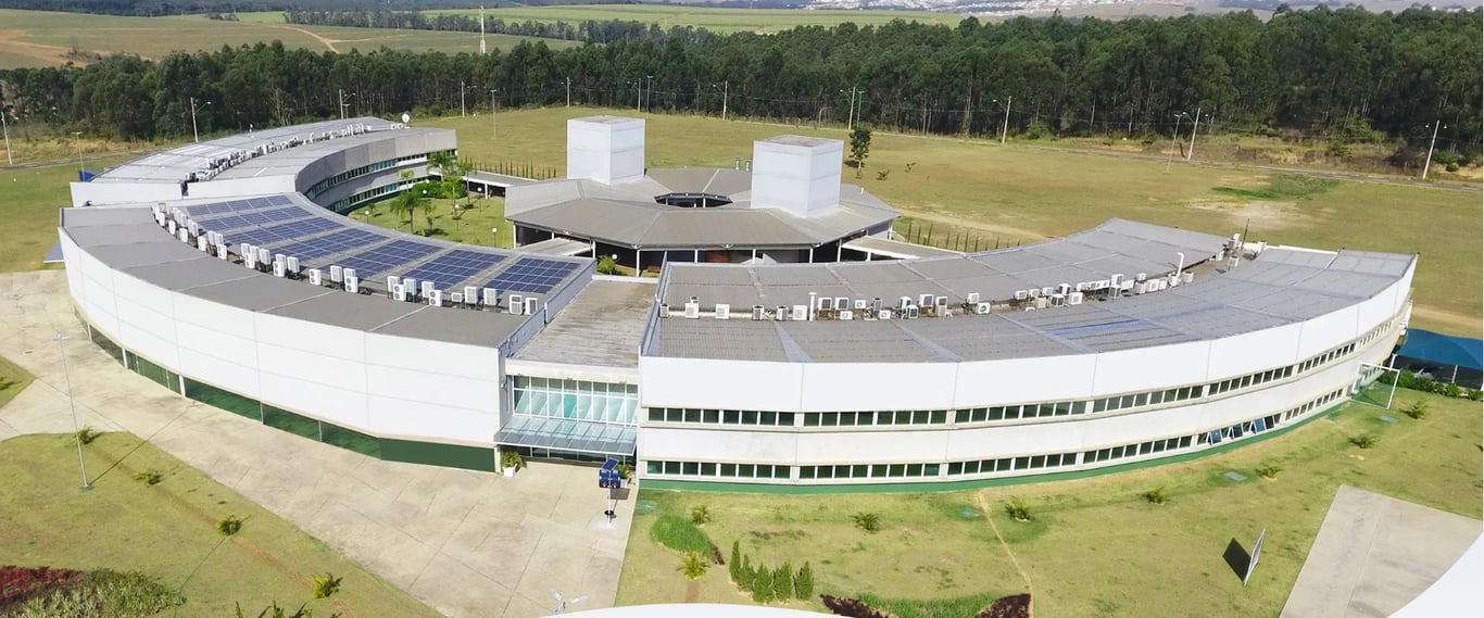 Vista aérea de edifício moderno com painéis solares, cercado por área verde